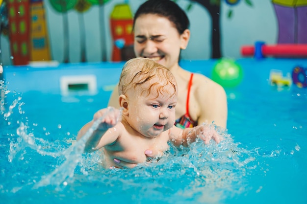 Treinamento de um recém-nascido na piscina com um treinador de natação Uma piscina para bebês Desenvolvimento infantil Uma criança pequena aprende a nadar na piscina