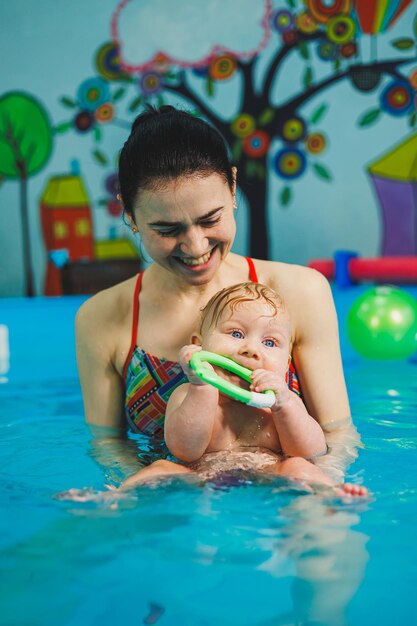 Treinamento de um recém-nascido na piscina com um treinador de natação Uma piscina para bebês Desenvolvimento infantil Uma criança pequena aprende a nadar na piscina