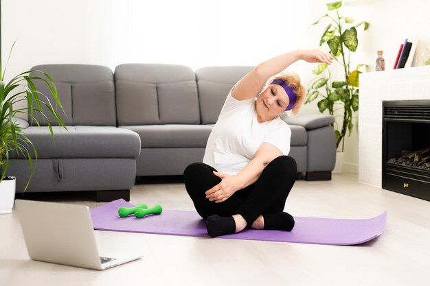 Treinamento Doméstico. Mulher sênior ativa fazendo exercício na frente do laptop em casa, espaço livre.