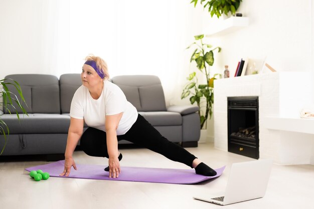 Treinamento Doméstico. Mulher sênior ativa fazendo exercício na frente do laptop em casa, espaço livre.