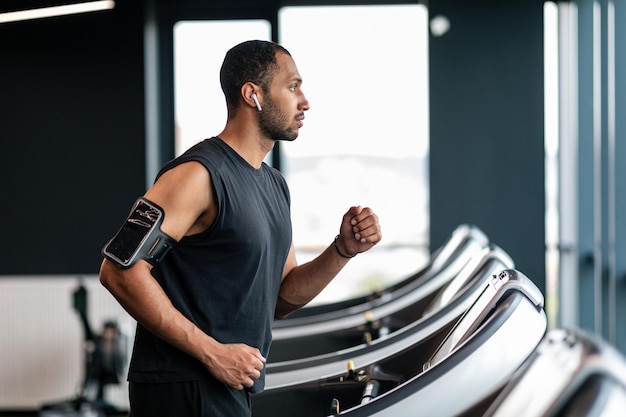 Treinamento esportivo motivado homem afro-americano usando esteira na academia