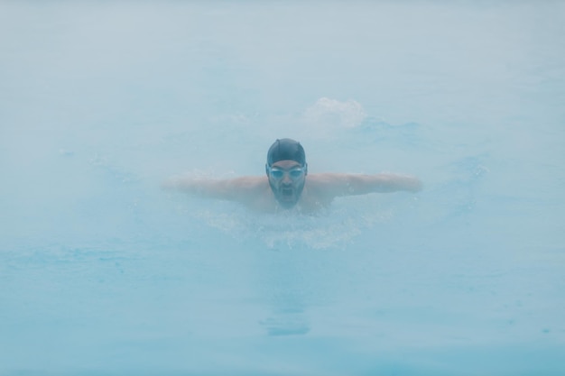 Treinamento masculino nadador apto nadar em piscina de inverno aberta com neblina Conceito de spa ao ar livre geotérmico