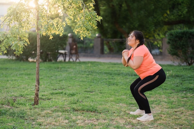 Treinamento no parque Pessoas obesas Estilo de vida ativo Corpo positivo Alegre motivado sorridente mulher obesa em roupas esportivas exercitando ao ar livre na primavera clima espaço vazio paisagem