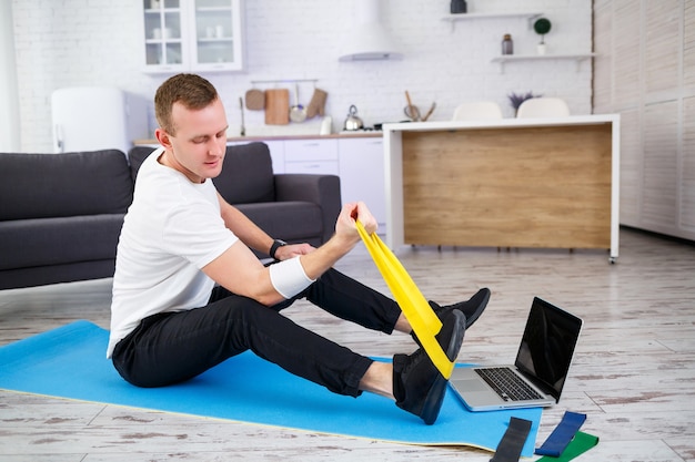 Treinamento on-line. Homem fazendo exercício com elásticos em casa, espaço livre. Praticando esportes em casa