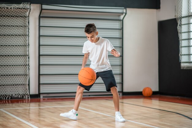 Treinamento. Um menino jogando basquete no ginásio e parecendo envolvido