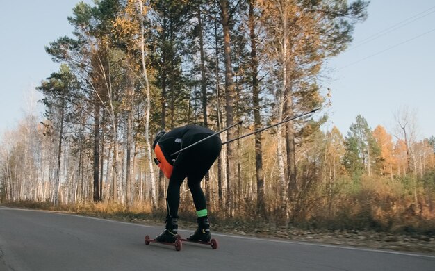 Foto treinando um atleta nos patinadores de patins passeio de biatlo nos esquis de rolo com bastões de esqui no capacete treino de outono esporte de rolo