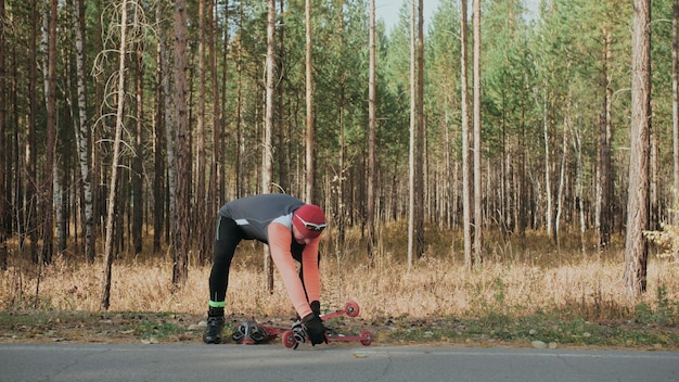 Foto treinando um atleta nos patinadores passeio de biatlo nos esquis com bastões de esqui no capacete treino de outono esporte de rolo homem adulto andando de patins o atleta faz o treino câmera lenta