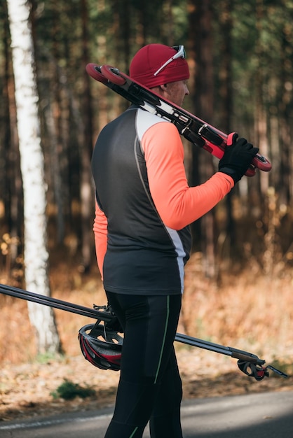 Treinando um atleta nos patinadores Passeio de biatlo nos esquis com bastões de esqui no capacete Treino de outono Esporte de rolo O atleta vai e segura equipamentos esportivos na mão