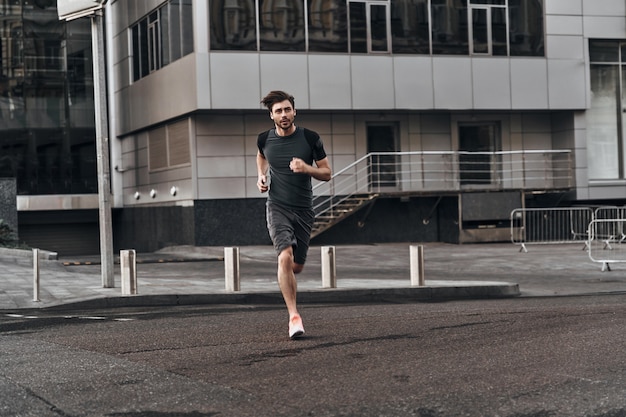 Treinar para ser o melhor. Comprimento total de um jovem bonito em roupas esportivas correndo pelas ruas da cidade