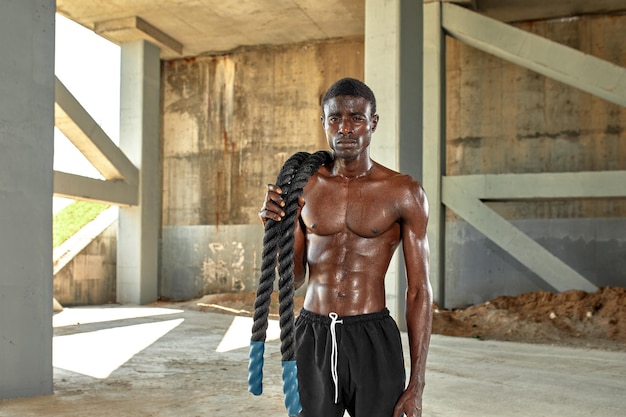 Treino de corda Homem esportivo fazendo exercícios de cordas de batalha ao ar livre Atleta masculino negro exercitando fazendo treinamento funcional com corda pesada