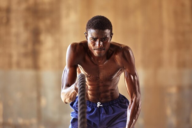 Treino de corda Homem esportivo fazendo exercícios de cordas de batalha ao ar livre Atleta masculino negro exercitando fazendo treinamento funcional com corda pesada