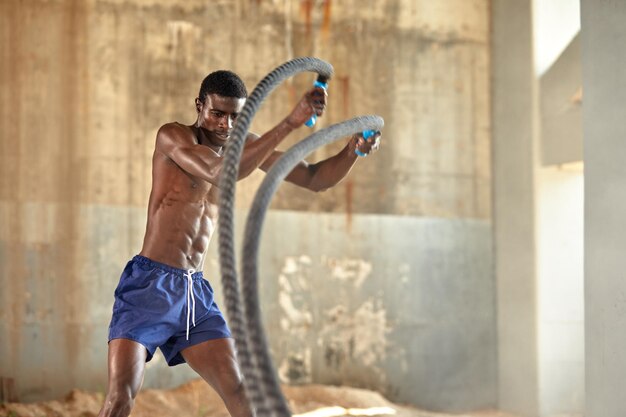 Treino de corda Homem esportivo fazendo exercícios de cordas de batalha ao ar livre Atleta masculino negro exercitando fazendo treinamento funcional com corda pesada