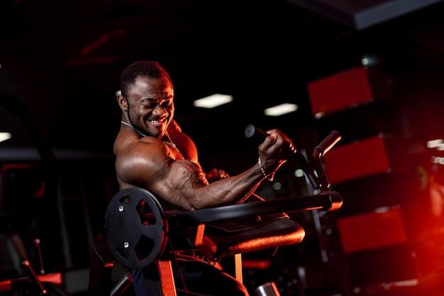Foto treino de força. determinado homem apto a se exercitar com halteres, bombeando os músculos sobre o fundo escuro do ginásio.