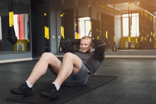 Treino de jovem alegre no clube de fitness. Retrato de um cara caucasiano fazendo exercícios, abdominais e abdominais, treinando dentro de casa na academia, copie o espaço