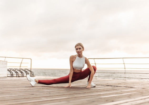 Treino matinal conceito de estilo de vida saudável mulher jovem e atraente em roupas esportivas faz alongamento das pernas antes do exercício