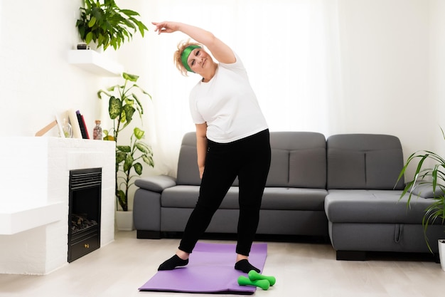 Treino matinal. Senhora sênior positiva aquecendo as mãos em casa, espaço vazio.