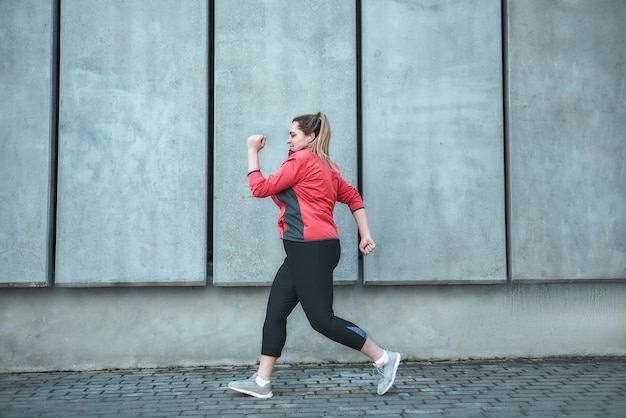 Treino matinal. Vista lateral do jovem plus size mulher em roupas de esporte correndo ao ar livre. Estilo de vida saudável. Perda de peso. Conceito de esporte