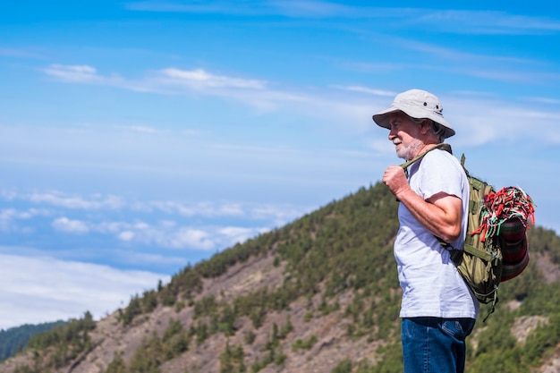 Trekker adulto solitário com uma mochila em pé e olhando a bela paisagem nas montanhas - trekking e caminhadas para pessoas maduras em atividades de lazer ao ar livre