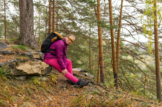 Trekker mujer sentada en un sendero de montaña y aferrándose a una rodilla adolorida