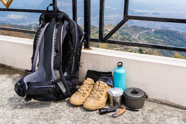 Trekking- oder Wanderausrüstung - Rucksack, Stiefel, Socken, Klappmesser, Gasbrenner, Wasserflasche, Wasserkocher und Taschenlampe. Konzept für Outdoor-Aktivitäten. Stillleben hautnah stockfoto.