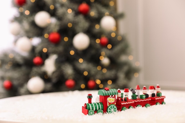 Trem de brinquedo brilhante na neve artificial na sala com árvore de Natal