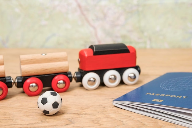 trem de brinquedo vermelho e bola de futebol perto de um passaporte biométrico deitado sobre uma velha mesa de madeira contra um mapa