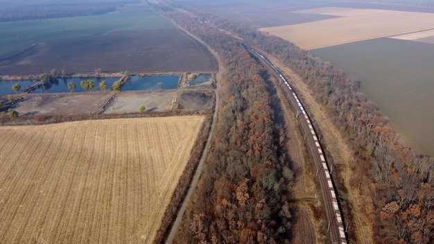 Trem de carga em movimento panorâmico ao longo de trilhos ferroviários árvores campos agrícolas