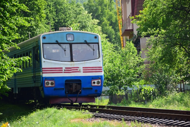 El tren eléctrico sale desde lejos de detrás de los árboles hasta la estación de tren.