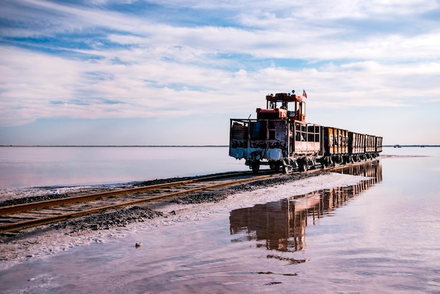 El tren viaja desde el agua Sal extraída en el lago Burlin Altai Rusia Bursolith Viejos viajes en tren en el ferrocarril colocado en el agua a través del lago salado