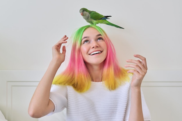 Trendig modisch mit bunter Frisur Teenager mit grünem jungen Papageienquaker auf dem Kopf, Freundschaft von Teenager-Mädchen und Vogel, Lebensstil von Teenager und Haustier
