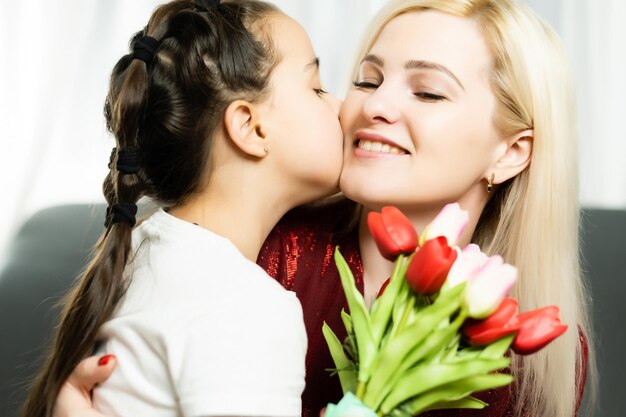 Trendige, attraktive, fröhliche Mutter und Tochter, die zusammen Urlaub genießen und einen großen, makellosen, saisonalen, farbenfrohen Strauß Tulpen haben, Komfort, Vergnügen, Freude, Genusskonzept auf grauem Hintergrund