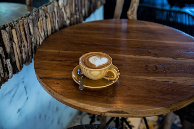 Trendige gelbe Tasse heißen Cappuccino auf Holztischhintergrund Latte Art in Herzform für Symbol der Liebe