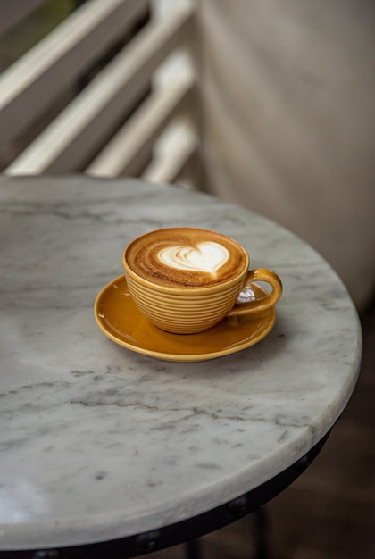 Trendige gelbe Tasse heißen Cappuccino auf Marmortischhintergrund Latte Art in Herzform für Symbol der Liebe