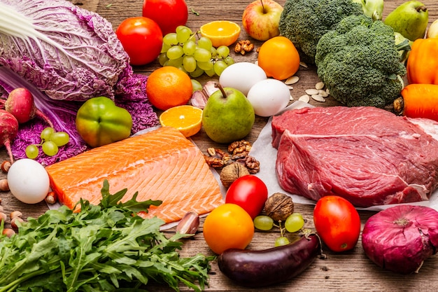 Foto trendige paläo / pegane ernährung. gesundes ausgeglichenes nahrungsmittelkonzept. set aus frischen produkten, rohem fleisch, lachs, gemüse und obst