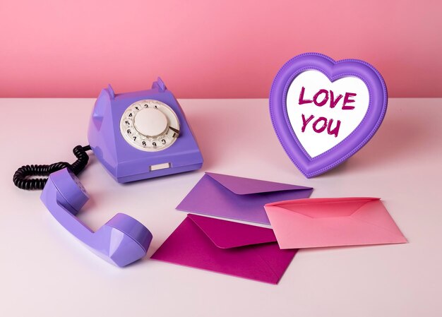 Trendige Valentinstagskomposition aus niedlichen rosa und violetten Objekten. Retro-Telefon, Liebesumschlag und herzförmiger Spiegel mit Liebesworten. Foto in hoher Qualität