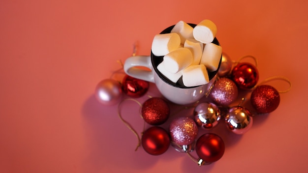 Trendiger Weihnachtshintergrund von heißer Schokolade mit Marshmallow, verziert mit Kugeln auf Rosa - Draufsicht