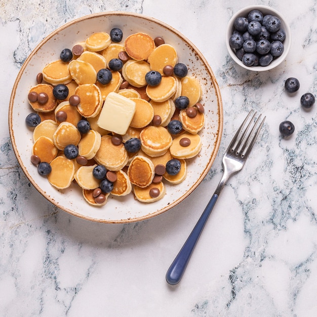 Trendiges Frühstück mit Minipfannkuchen, Blaubeeren und Schokoladenstückchen, Draufsicht.