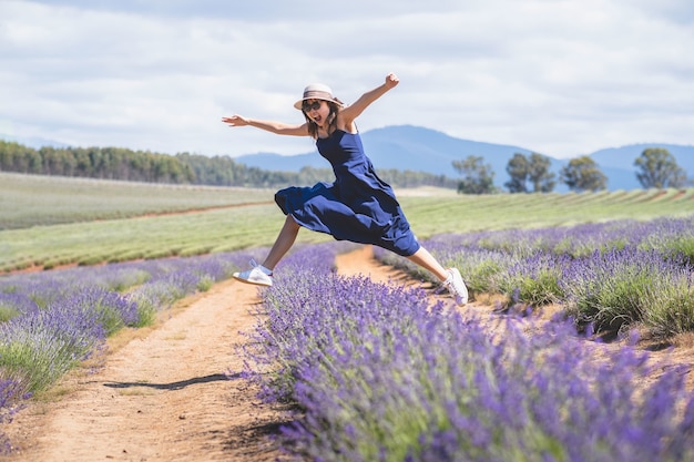 Trendiges junges Mädchen mit Sonnenbrille und weißem Hut springen über eine Reihe von Lavendelblüten