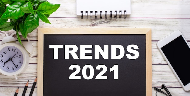 TRENDS 2021 escrito em uma parede preta perto de lápis, um smartphone, um bloco de notas branco e uma planta verde em um vaso