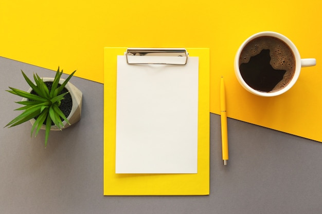 Trendy Arbeitsplatz mit Zwischenablage Stift Smartphone Tasse Kaffee und saftige Pflanze auf gelben und grauen Bürotisch Schreibtisch