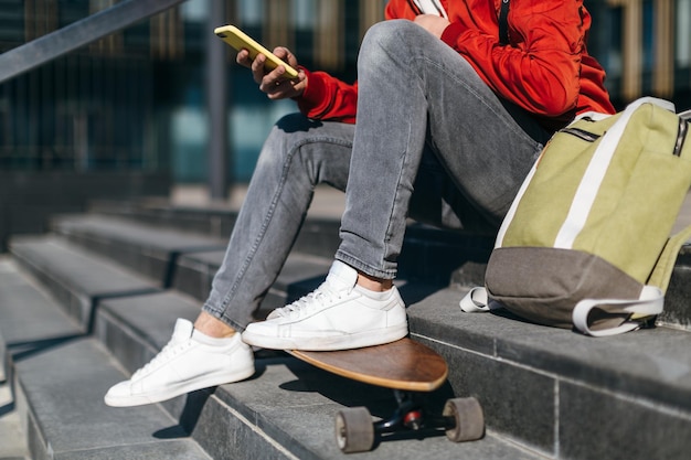 trendy Hipster mit Longboard sitzt auf der Treppe Mann plaudert am Handy