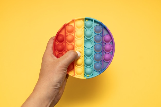 Trendy Rainbow Pop it Anti-Stress-Spielzeug zappeln, drücken Sie es in Kinderhände. Ansicht von oben