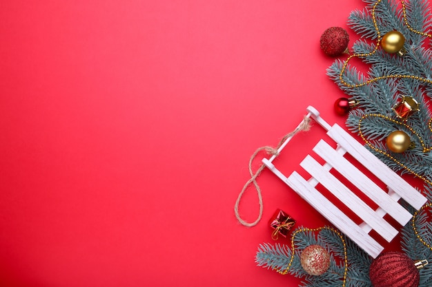 Trenó de brinquedo de Natal com galho de árvore do abeto, sobre um fundo vermelho