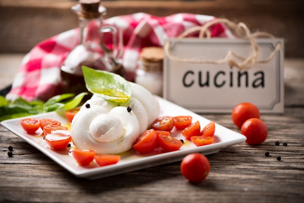 Trenza de mozzarella servida con tomates en un plato blanco con fondo de madera