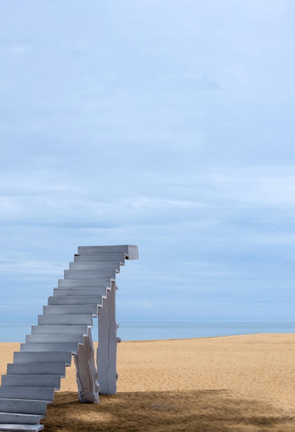 Treppe zum Himmel am Strand an sonnigen Sommertagen. Weiße Holztreppe am braunen Sandstrand mit klarem blauen Himmel und Wolkenlandschaft am Meer mit Platz für Text