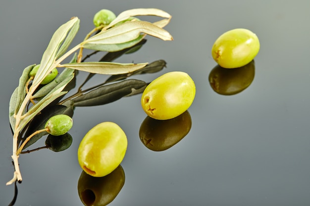 Tres aceitunas con rama de olivo con frutas sobre un fondo gris