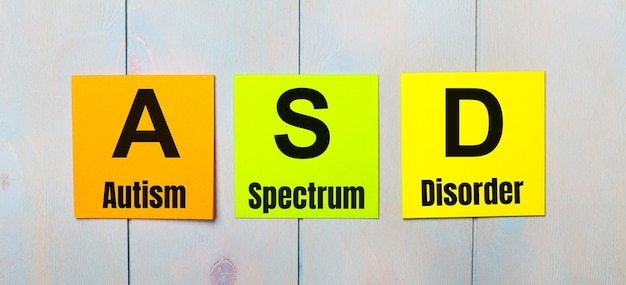 Três adesivos coloridos com o texto ASD Autism Spectrum Disorder e um fundo de madeira azul claro