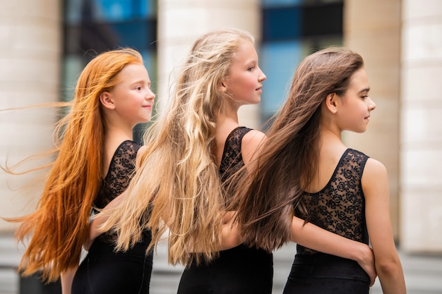 Tres adolescentes con cabello suelto, pelirroja rubia y morena, de pie de perfil afuera en verano. Los vloses se desarrollan con el viento.