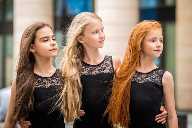 Três adolescentes com cabelos soltos, loira, ruiva e morena, perfilam-se do lado de fora no verão. Vloses se desenvolvem no vento.