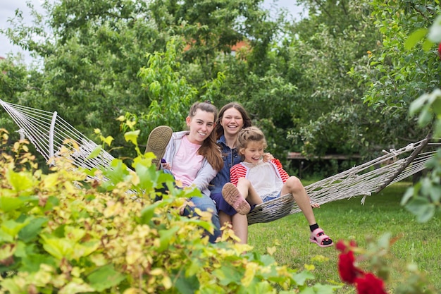 Foto três adolescentes e uma criança se divertindo rindo em uma rede em um jardim